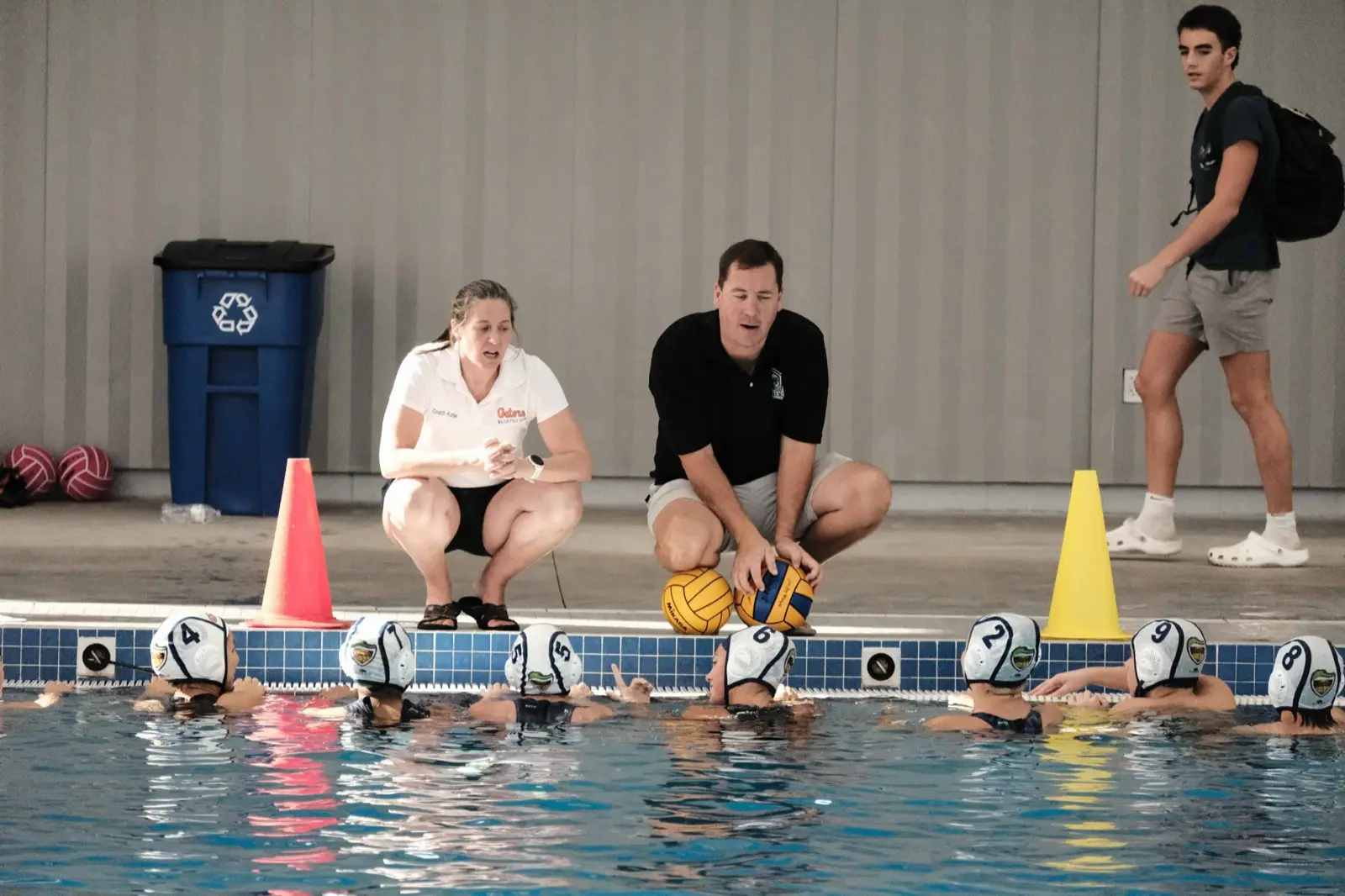 Two coaches crouched on the deck briefing the team in the water