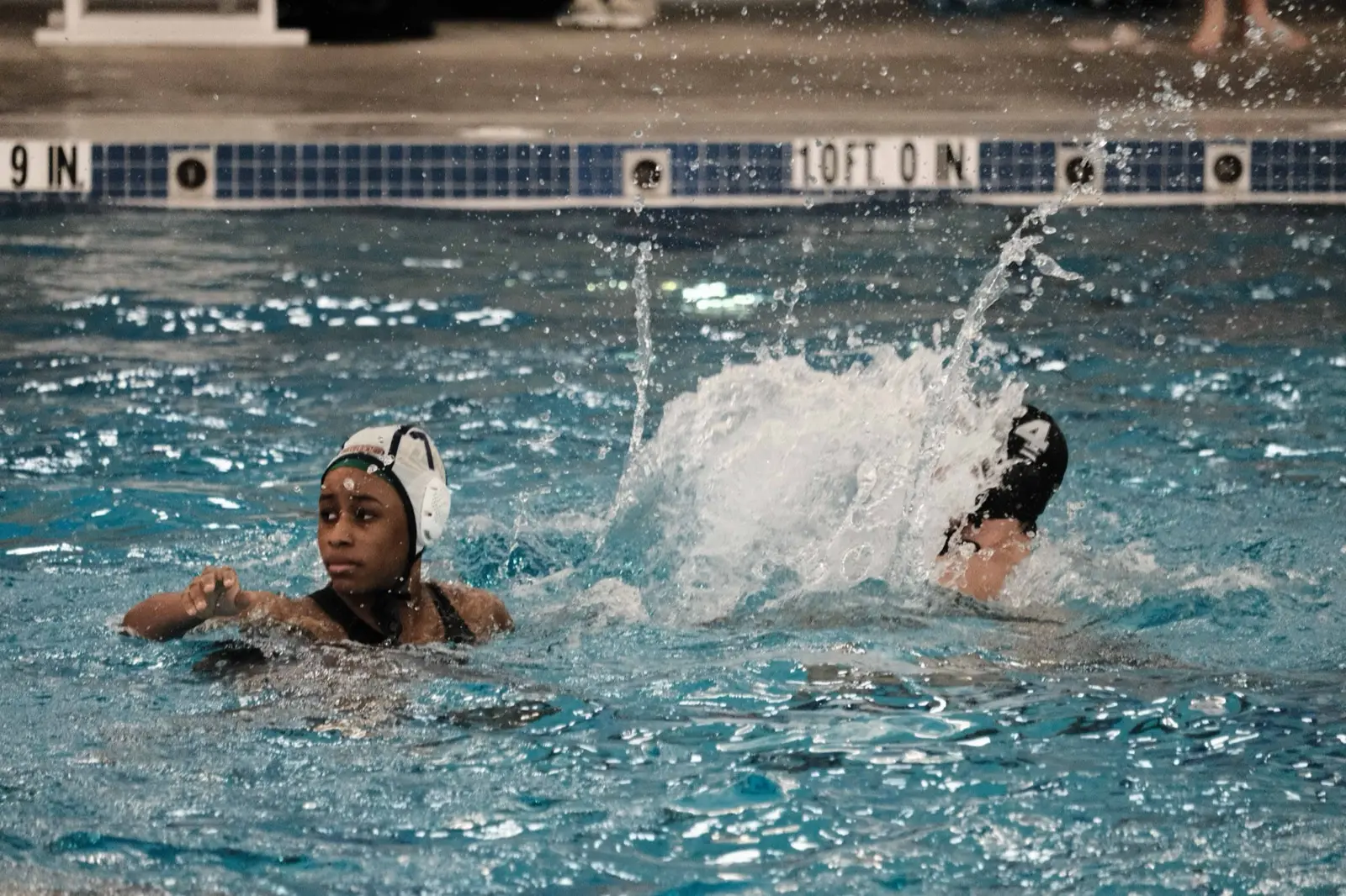 Two athletes in white caps racing through a splash