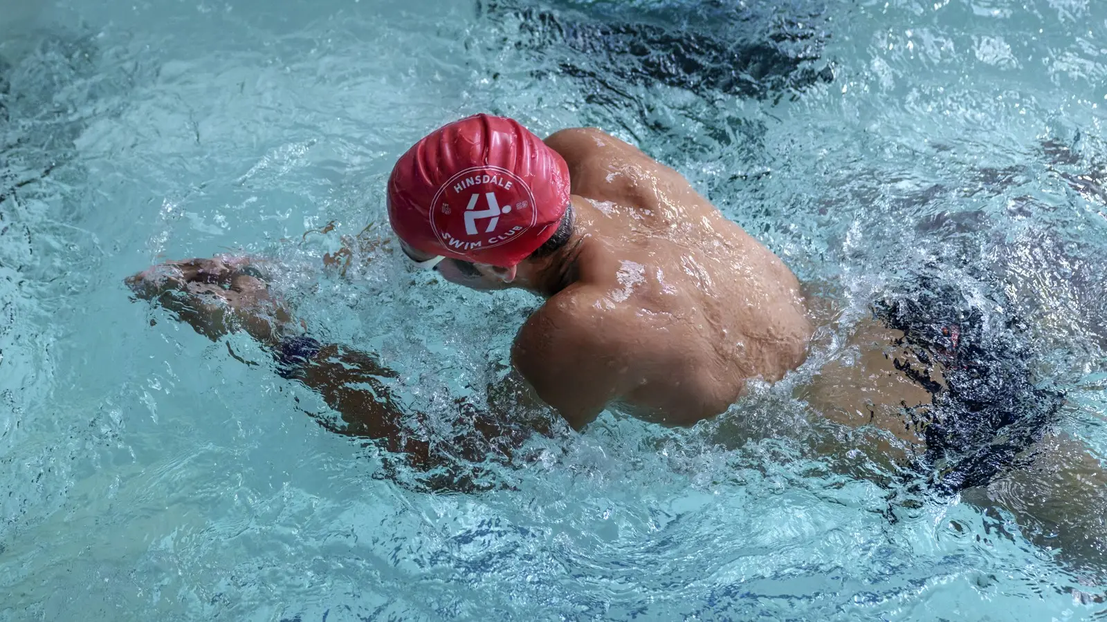 An adult swimmer in a red cap swimming freestyle