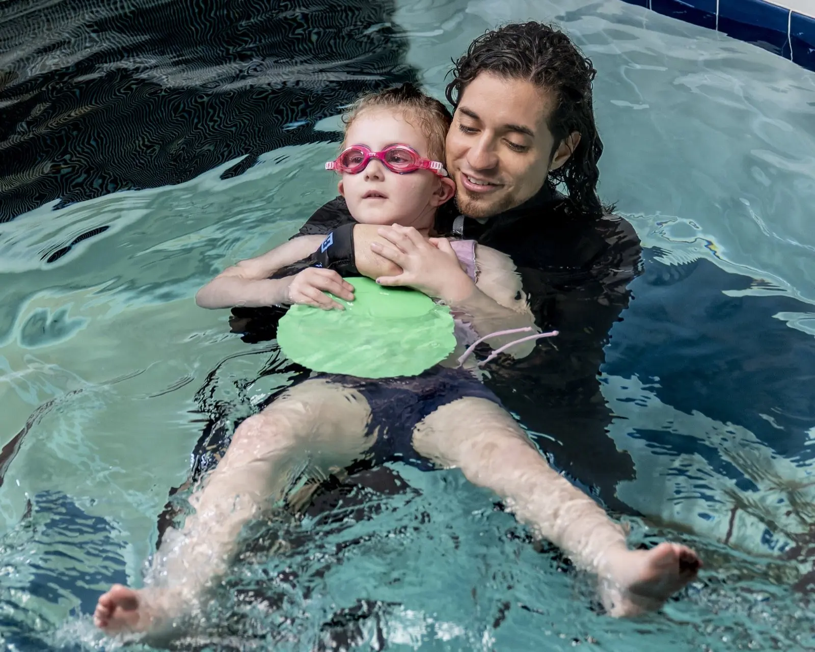 An instructor supporting a young swimmer in a back float on a kickboard