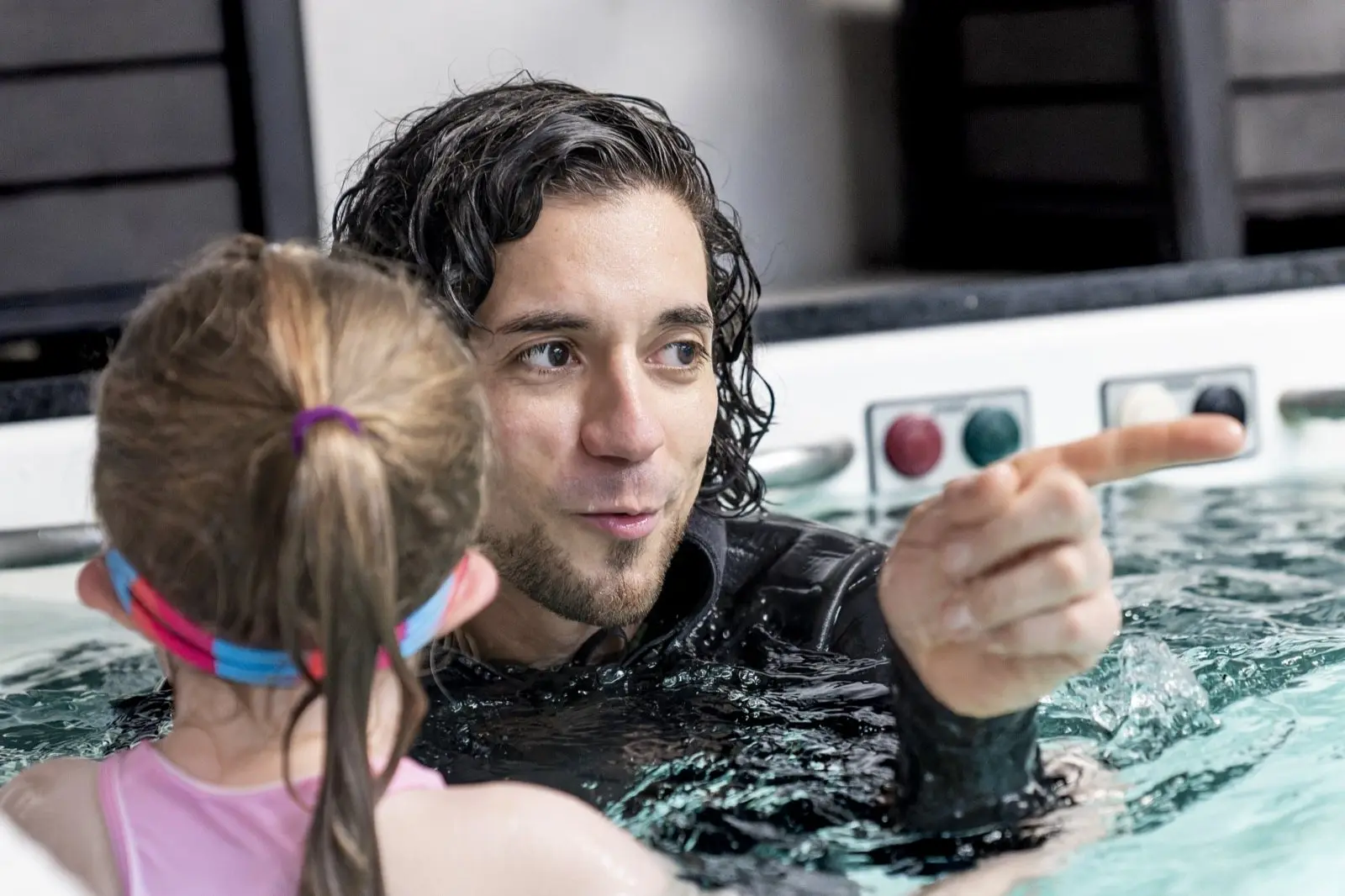 An instructor in the water pointing out the next skill to a young swimmer