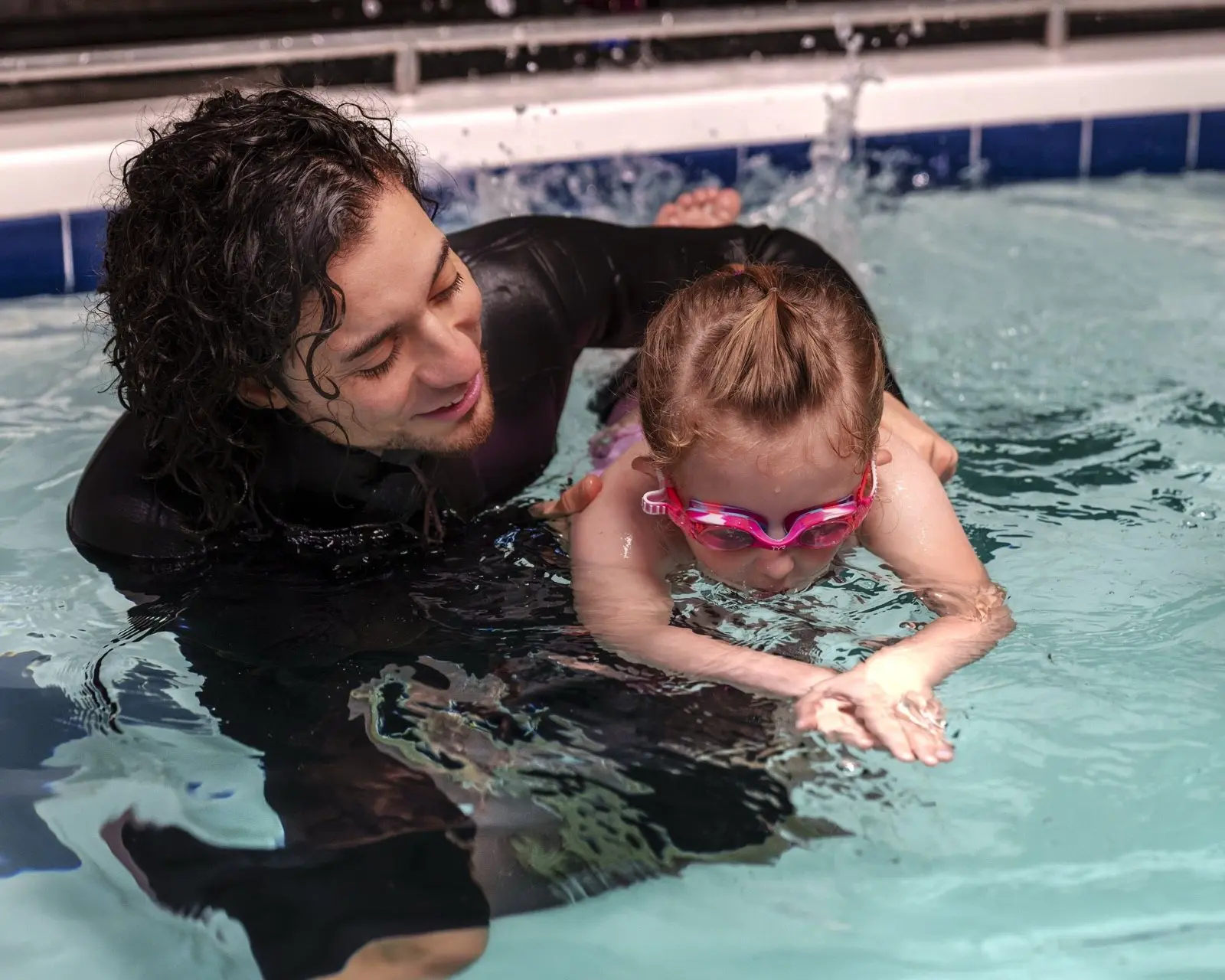 An instructor supporting a young swimmer through her first front crawl strokes
