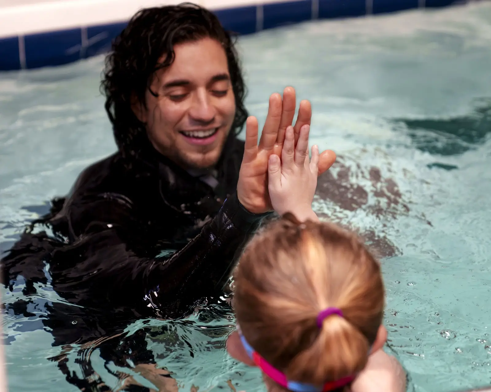 An instructor and a young swimmer sharing a high-five at the end of a skill