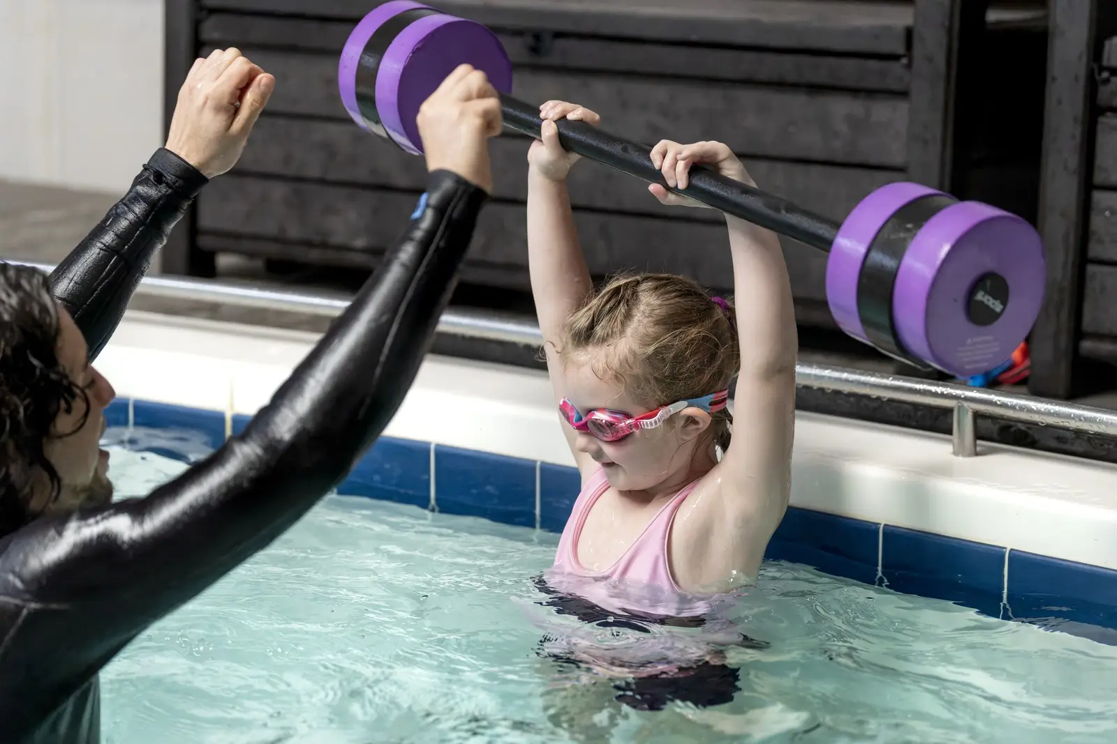 A young swimmer holding a float bar over her head