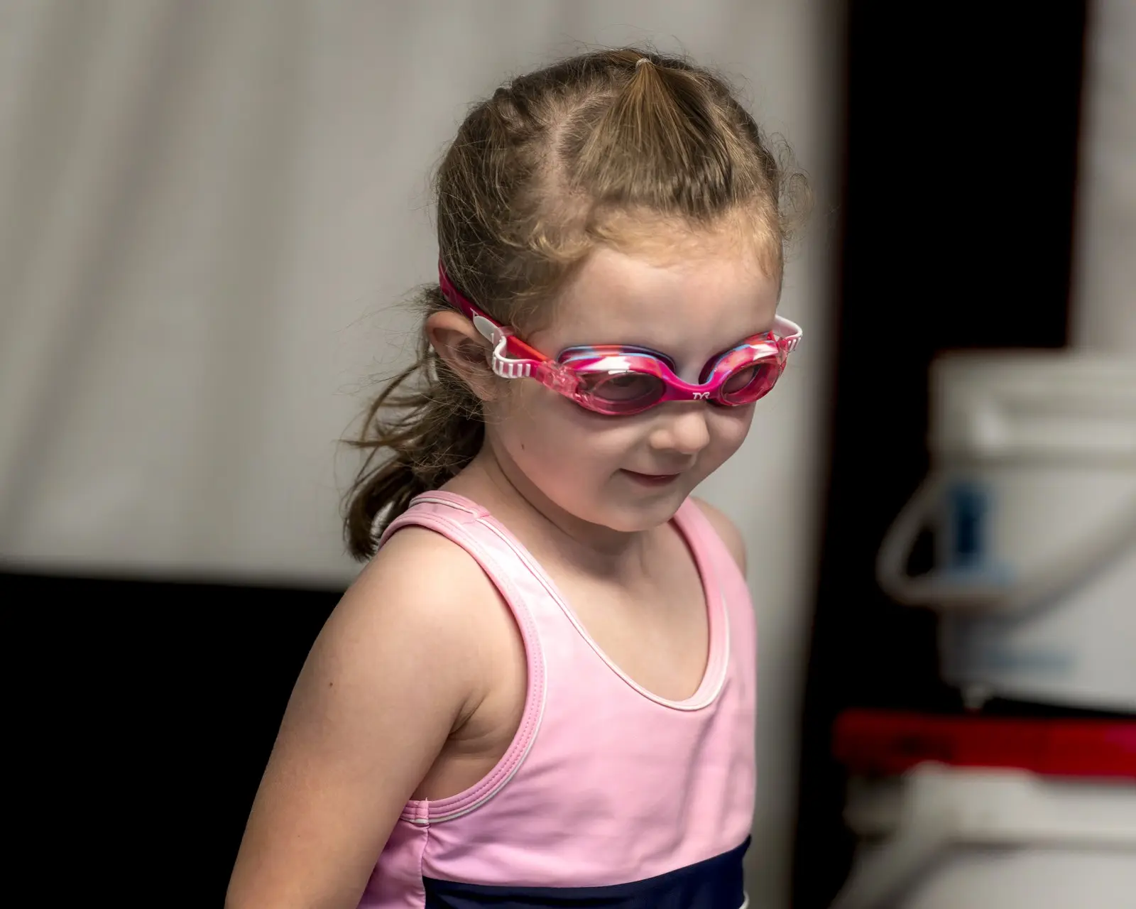 A young swimmer in pink goggles smiling before her lesson