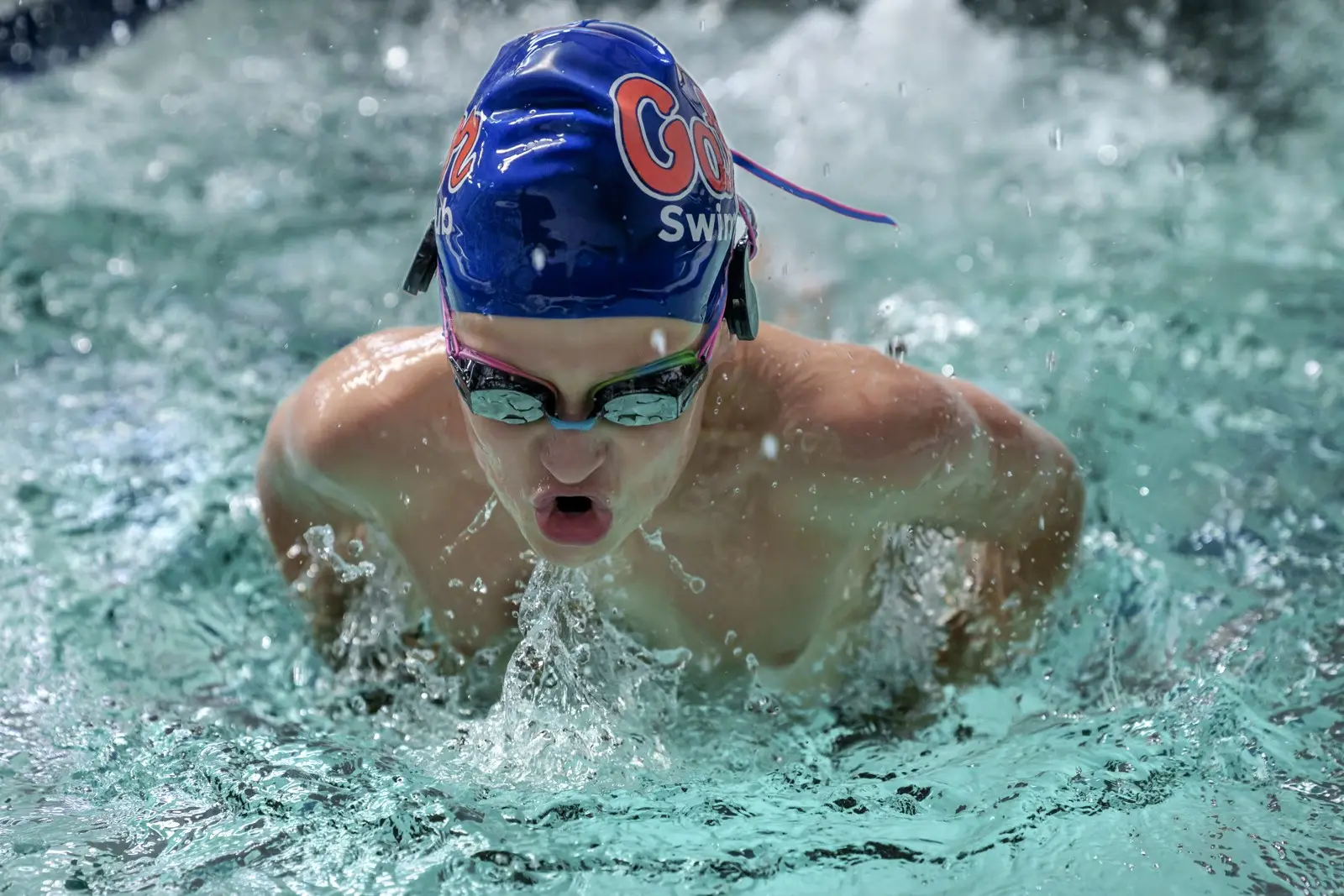 A teenage swimmer in a Gator Swim Club cap swimming butterfly
