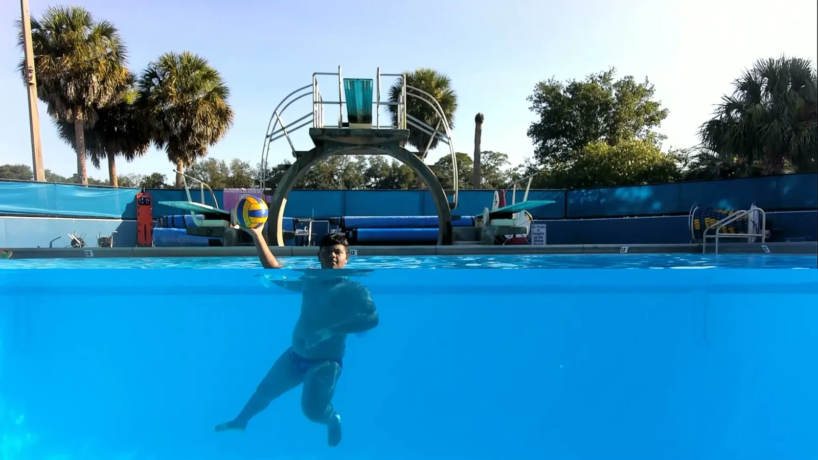 A split-level view of an athlete raising the ball to shoot, filmed above and below the water at the 2026 summer event